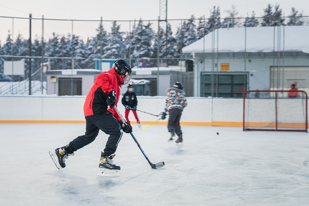 Kolme poikaa pelaamassa jääkiekkoa luistelukaukalossa talvella.